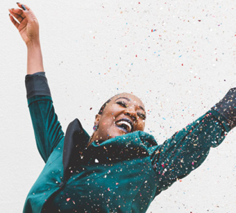 young black woman wearing a teal blazer dancing in a rain shower of confetti
