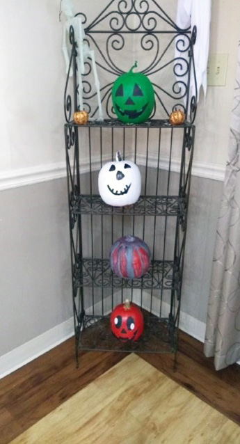 4 elaborately decorated pumpkins sitting on rod iron shelf