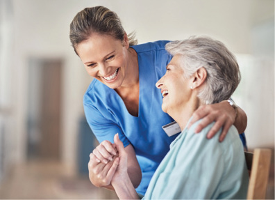 female nurse holding hands and laughing with senior woman sitting down