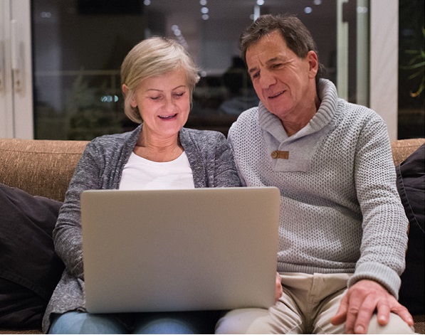 older adult man and woman sitting on sofa looking at laptop together